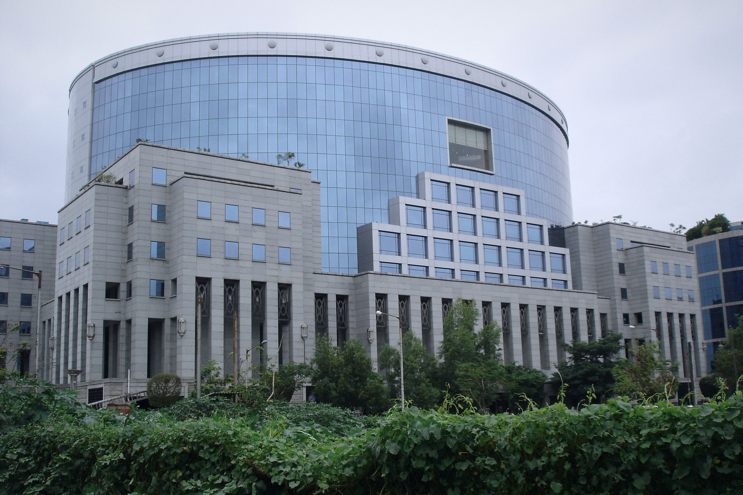 A curved glass office tower and stone colonnade in Bandra Kurla Complex, Mumbai, under a monsoon sky