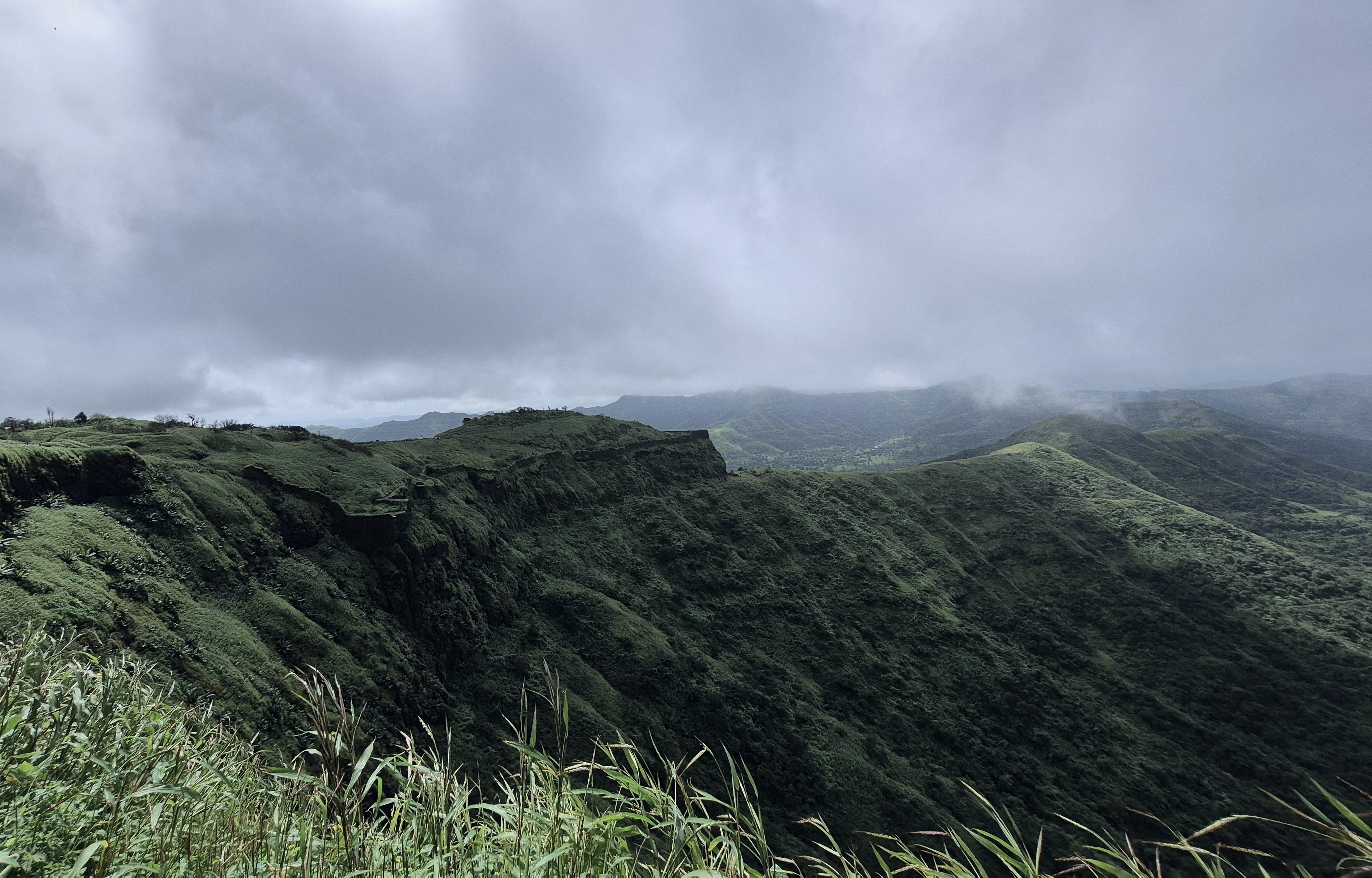 A green Sahyadri ridge near Pune under low monsoon cloud, an escarpment falling away to the valley