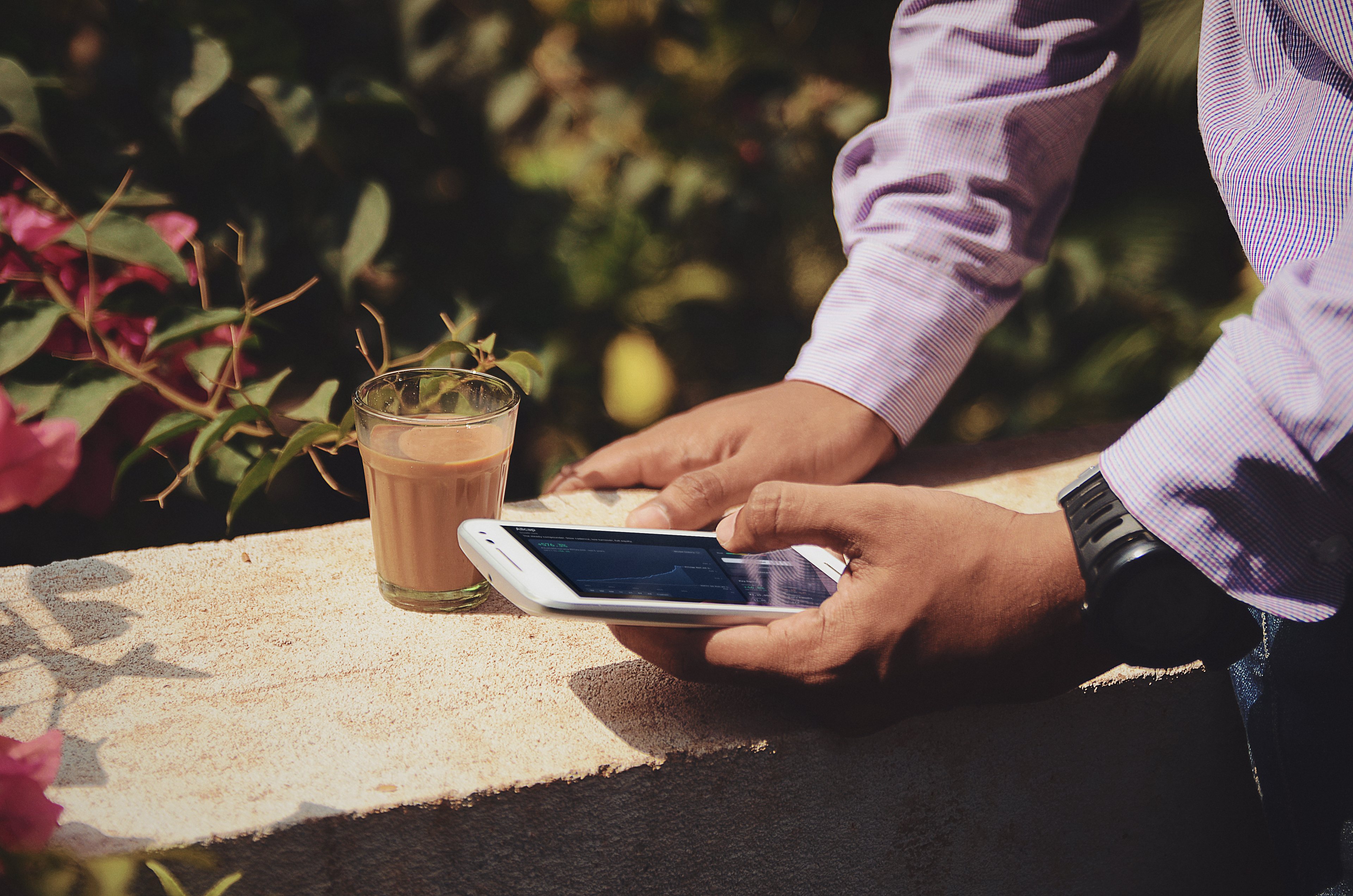 Hands hold a phone showing a RupeeCase strategy chart beside a glass of cutting chai on a sunlit ledge