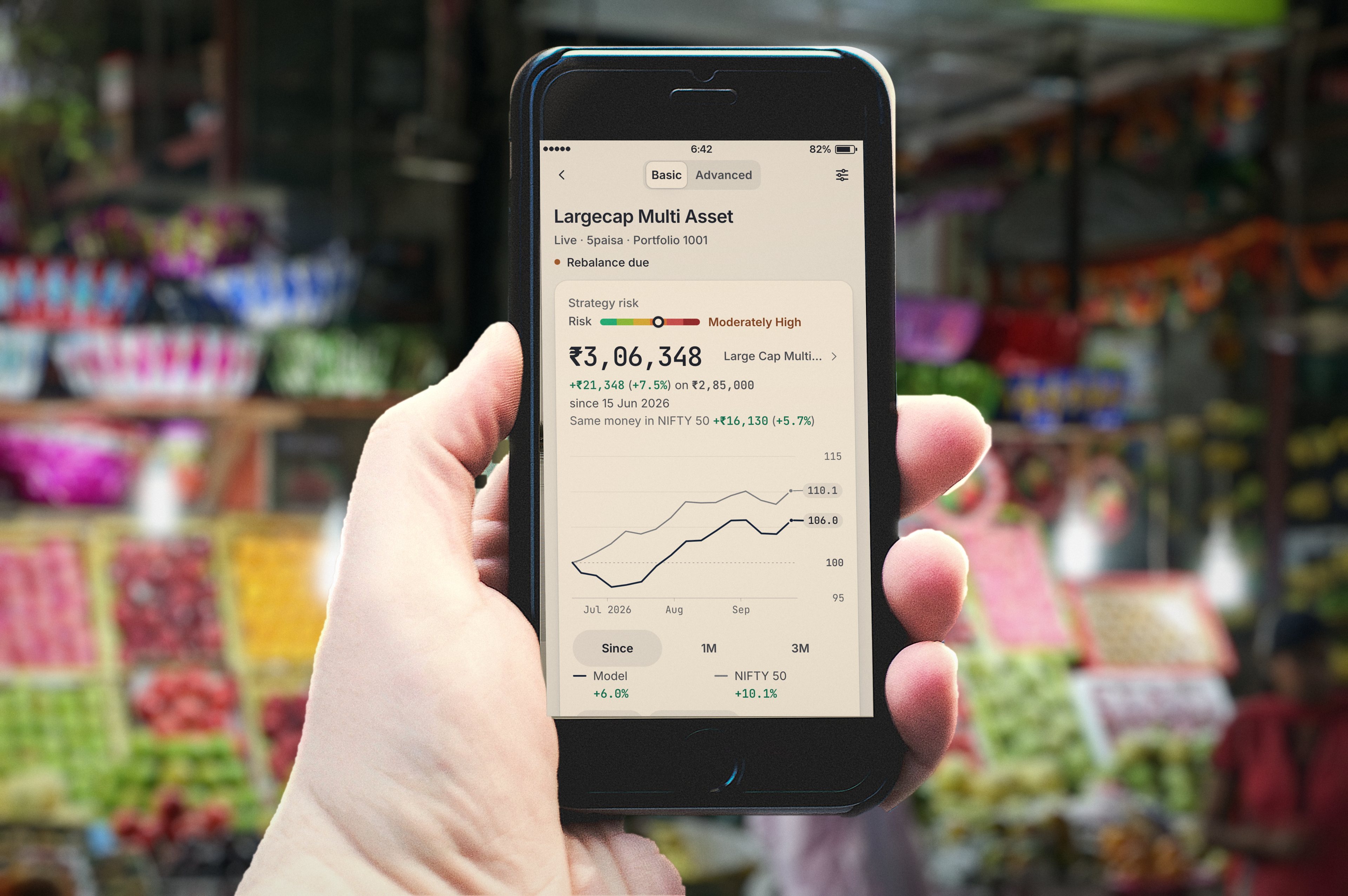 A hand holds a phone showing a RupeeCase sample portfolio in front of a fruit stall at Crawford Market, Mumbai