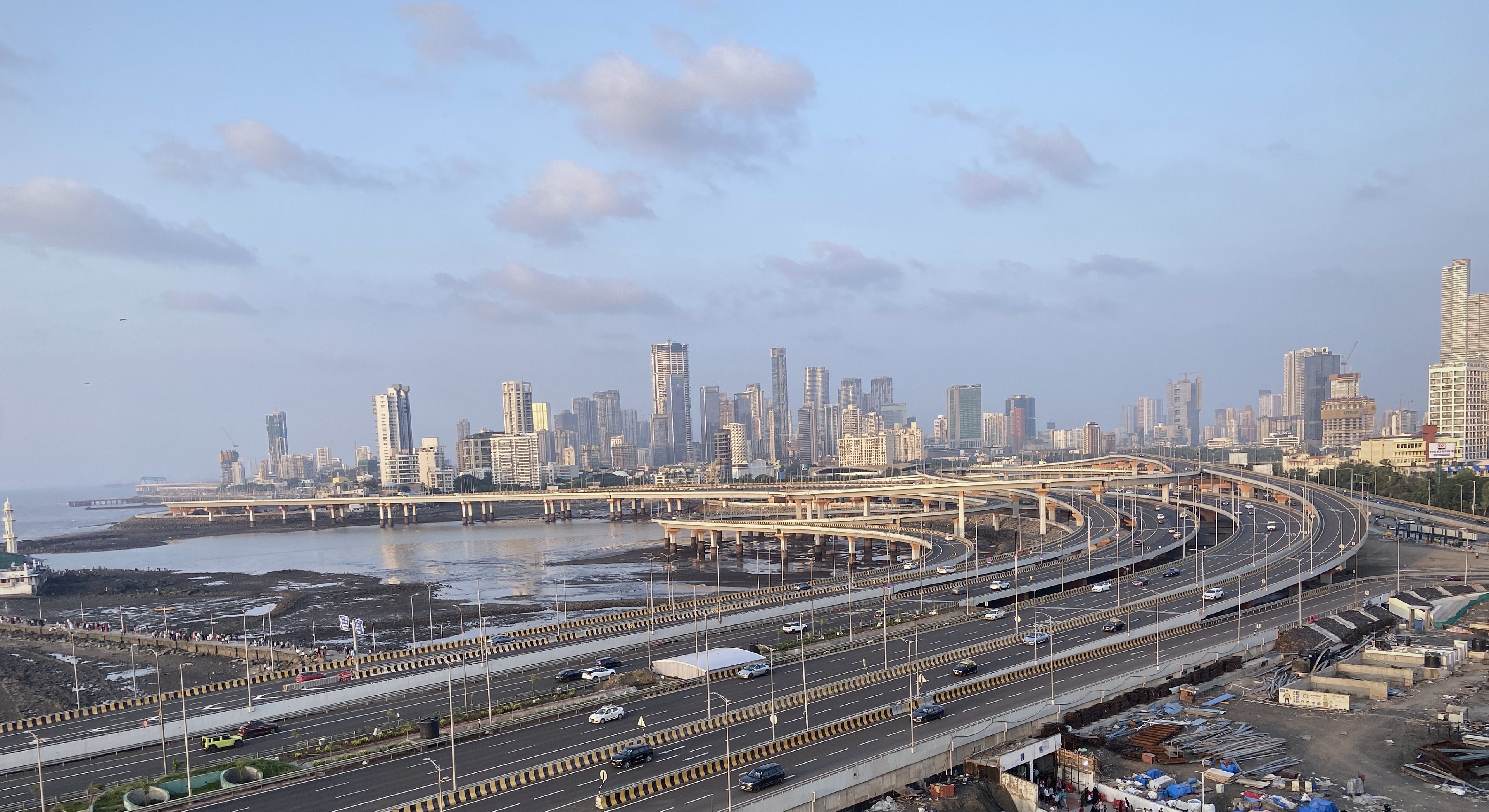 The Mumbai Coastal Road interchange in evening light, carriageways branching towards the Worli skyline