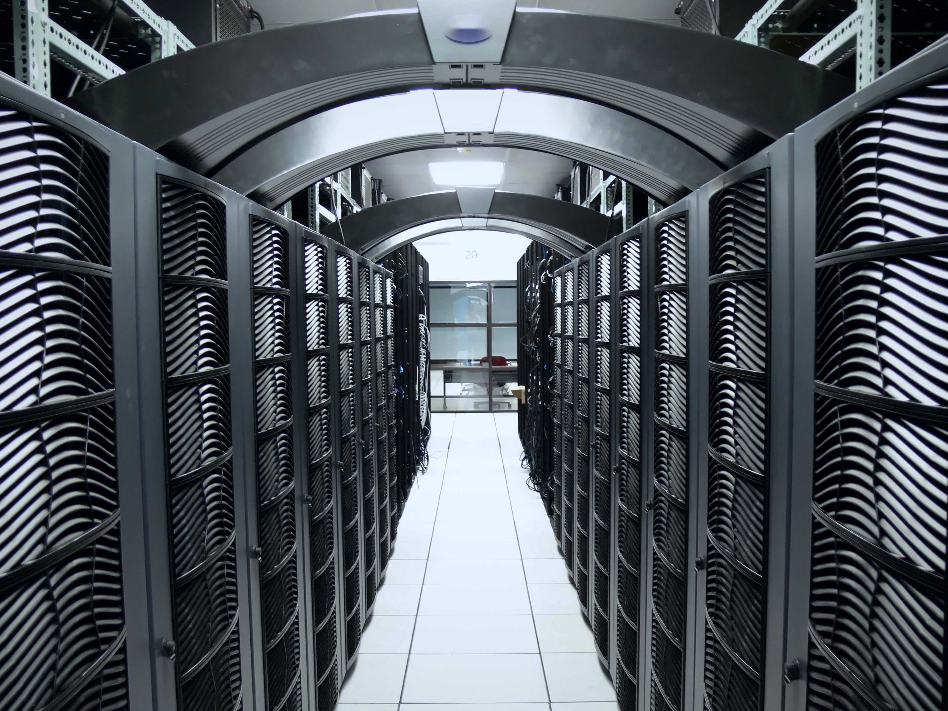 A data centre aisle between rows of server racks under arched light panels