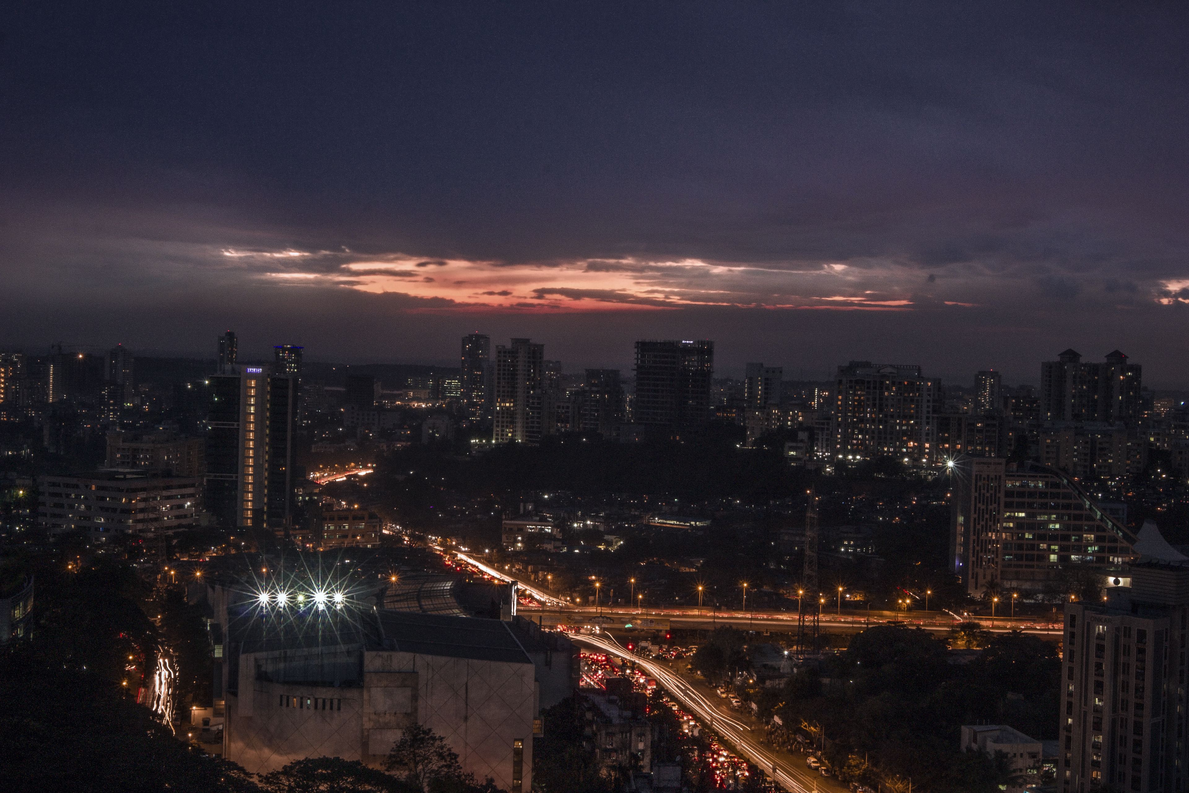 Mumbai at dusk from a high floor, towers under a dark sky and the evening traffic in streaks of light